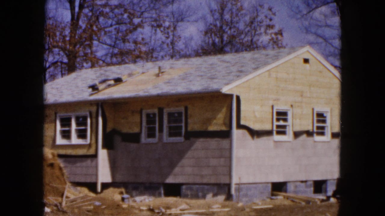Partly finished house exterior with gray lower siding, roof vents, windows, and bare trees.