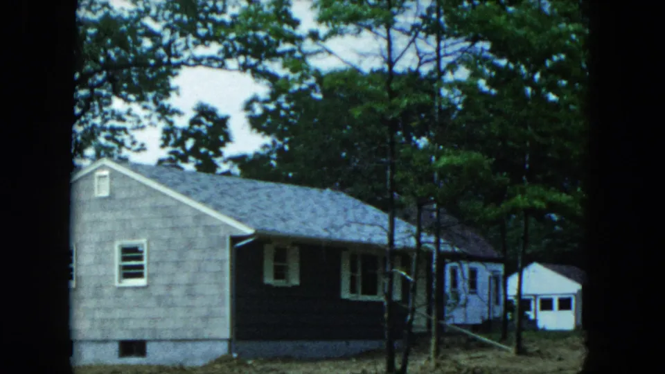 The pan reveals more of the Hicksville house exterior with a small white shed beyond the trees.
