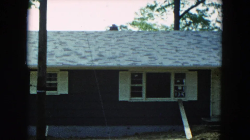 1954 Hicksville, New York frame showing the house roofline, dark siding, white shutters, and a partly hidden front window.