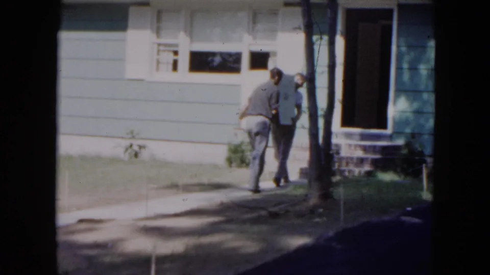 Two men approach the front doorway of the blue-sided Hicksville house while carrying the appliance in 1954 footage.