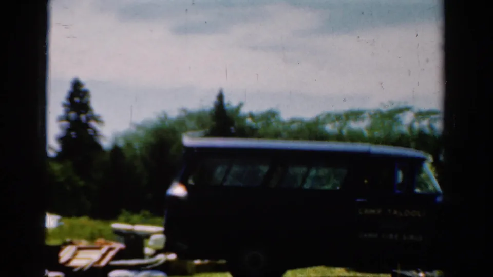 1954 California frame of a dark station wagon with camp lettering, parked in a sunny outdoor camp area.