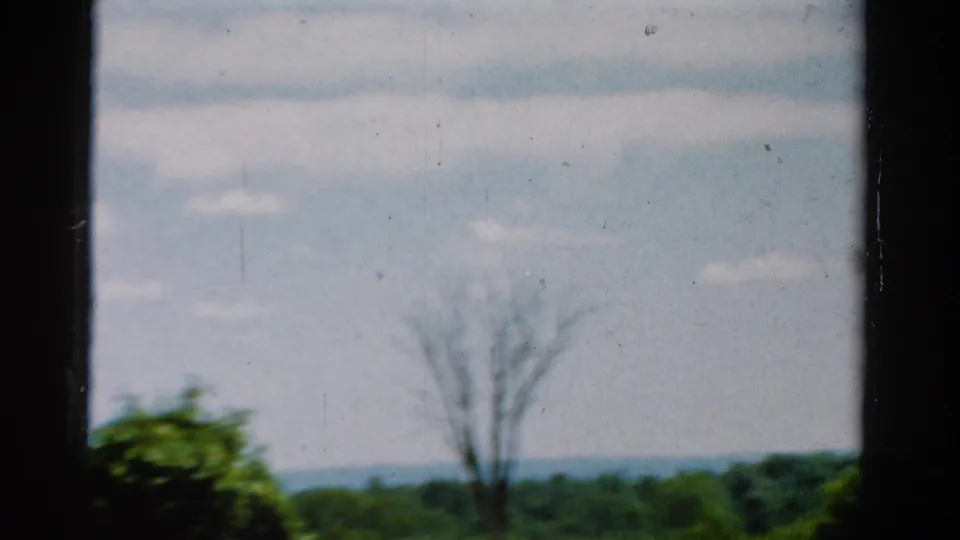 1954 California 8mm frame shifting away from the vehicle toward trees, distant hills, and open sky.