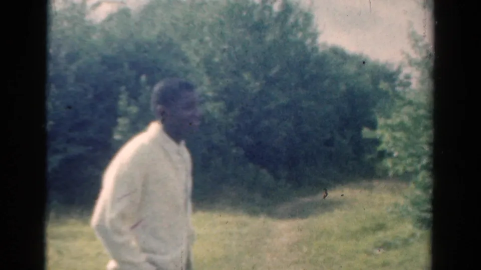 1954 California home-movie frame showing an adult man in a light shirt beside a wooded grassy area.