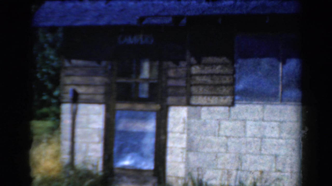 Closer view of the camp building front with a sign, window, door area, wood siding, and block wall.