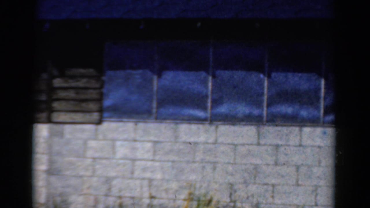 White cinder block wall below dark blue window panes, framed by black film borders.