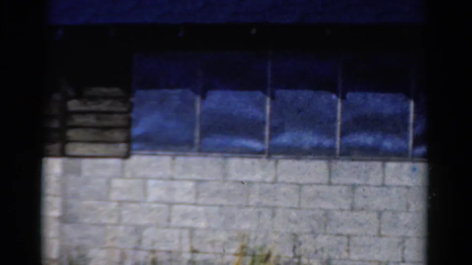 1954 California 8mm frame showing a white block wall beneath a row of dark blue-tinted windows with black projection borders.