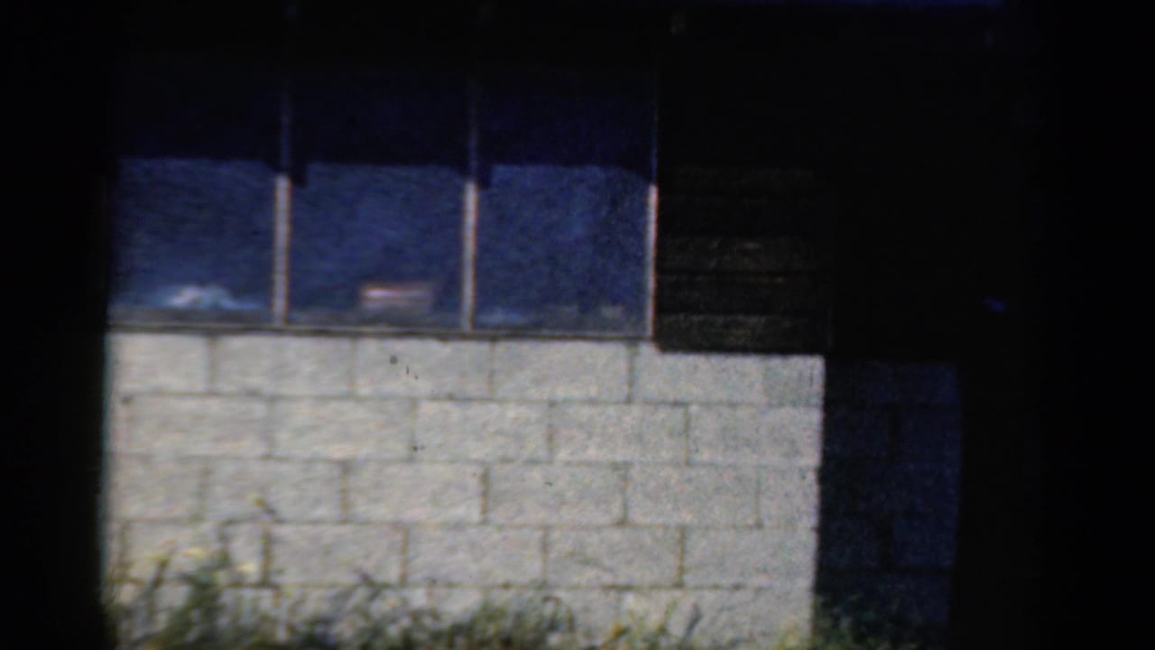 Wood-and-concrete camp building exterior with windows and grass at the base.