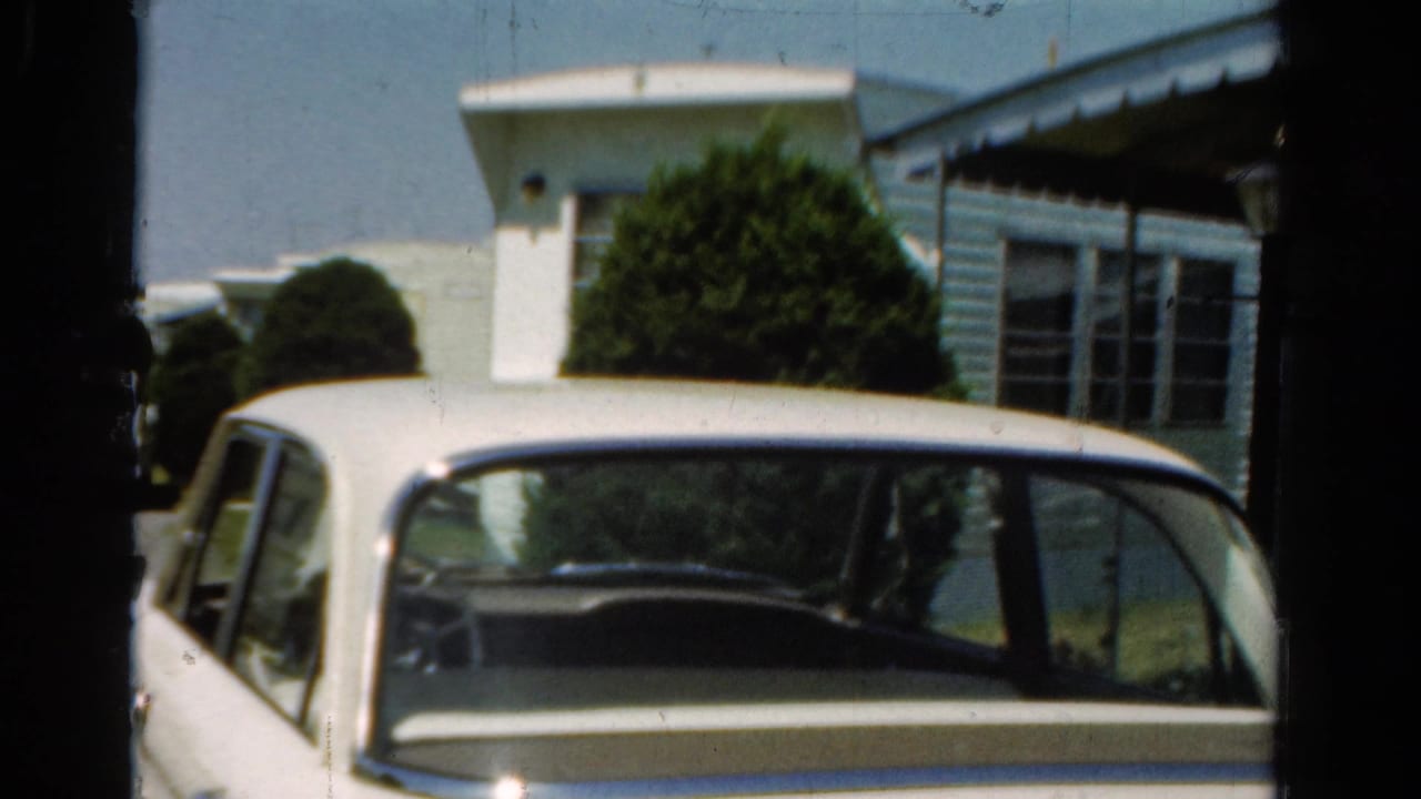 Parked white sedan in front of a low residential structure with windows and shrubs.