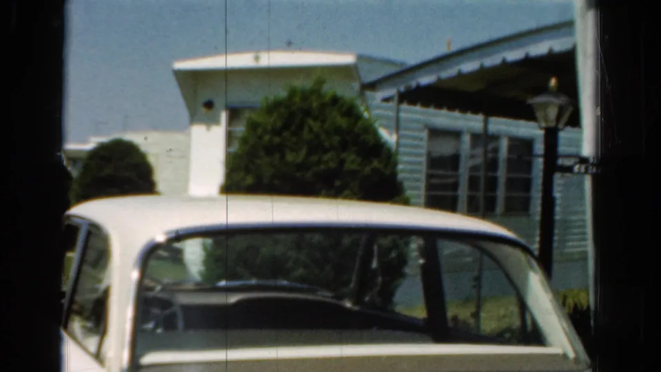Final frame of the static 1954 California shot, showing the parked white sedan near a mobile home in bright sun.