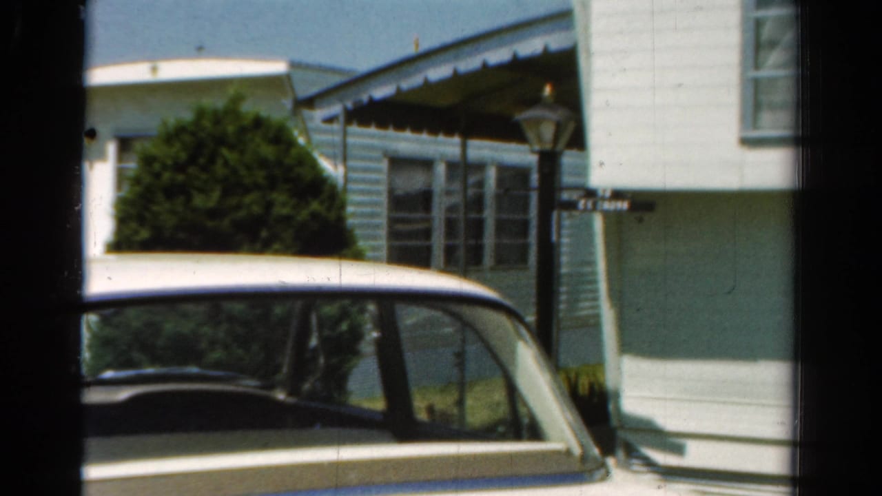Parked car seen beside a white and blue mobile home in bright daylight.