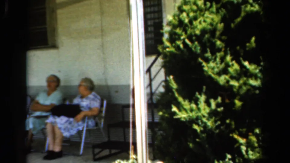 The porch scene continues with two elderly women seated in shade, viewed through a dark frame with greenery filling the right side.