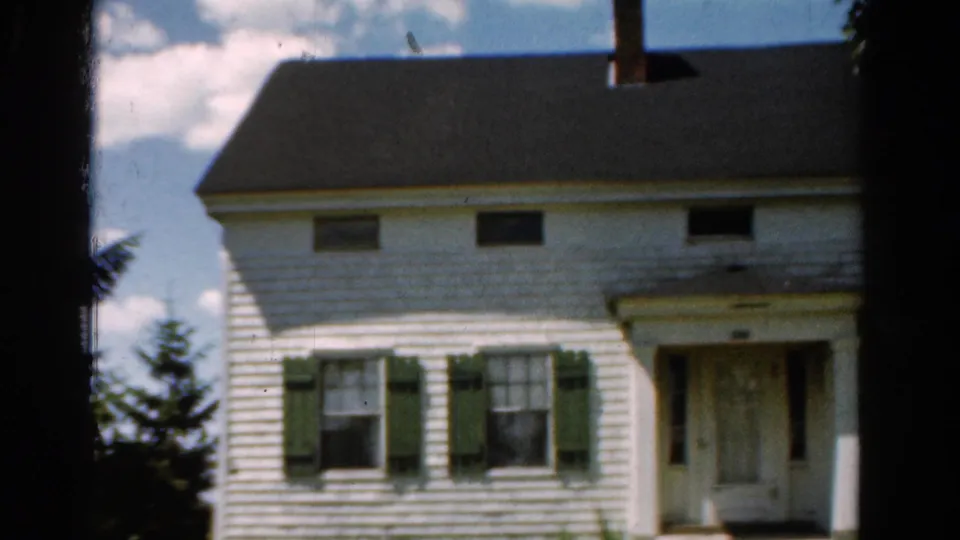 1954 California exterior view of a white house facade, green shutters, dark roofline, front door, and bright sky.