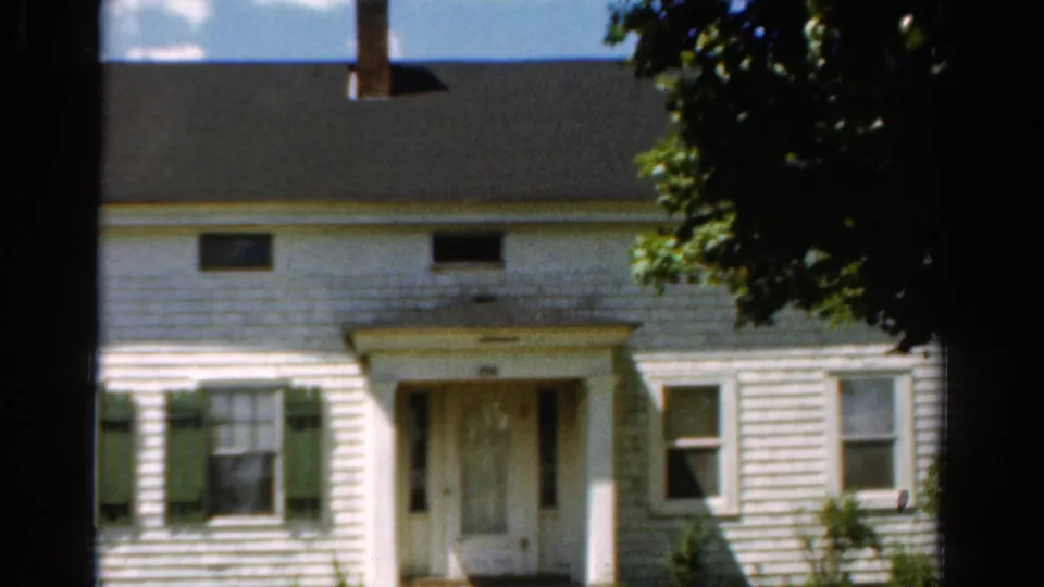 Final 1954 California frame showing the farmhouse exterior with green shutters, central entry, dark roof, chimney, and tree shade on the right.