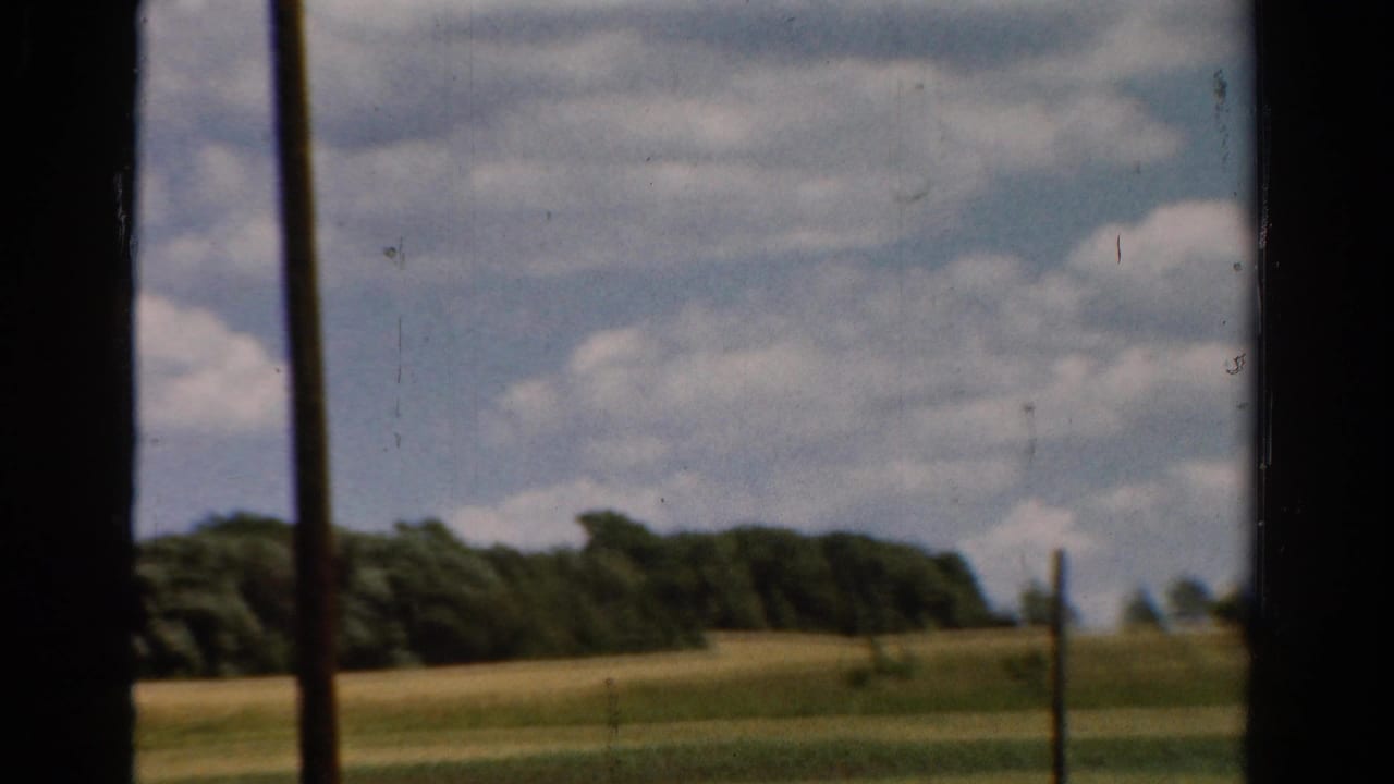 1954 California 8mm view of open fields, treeline, and scattered clouds, partially blocked by dark vertical window framing.