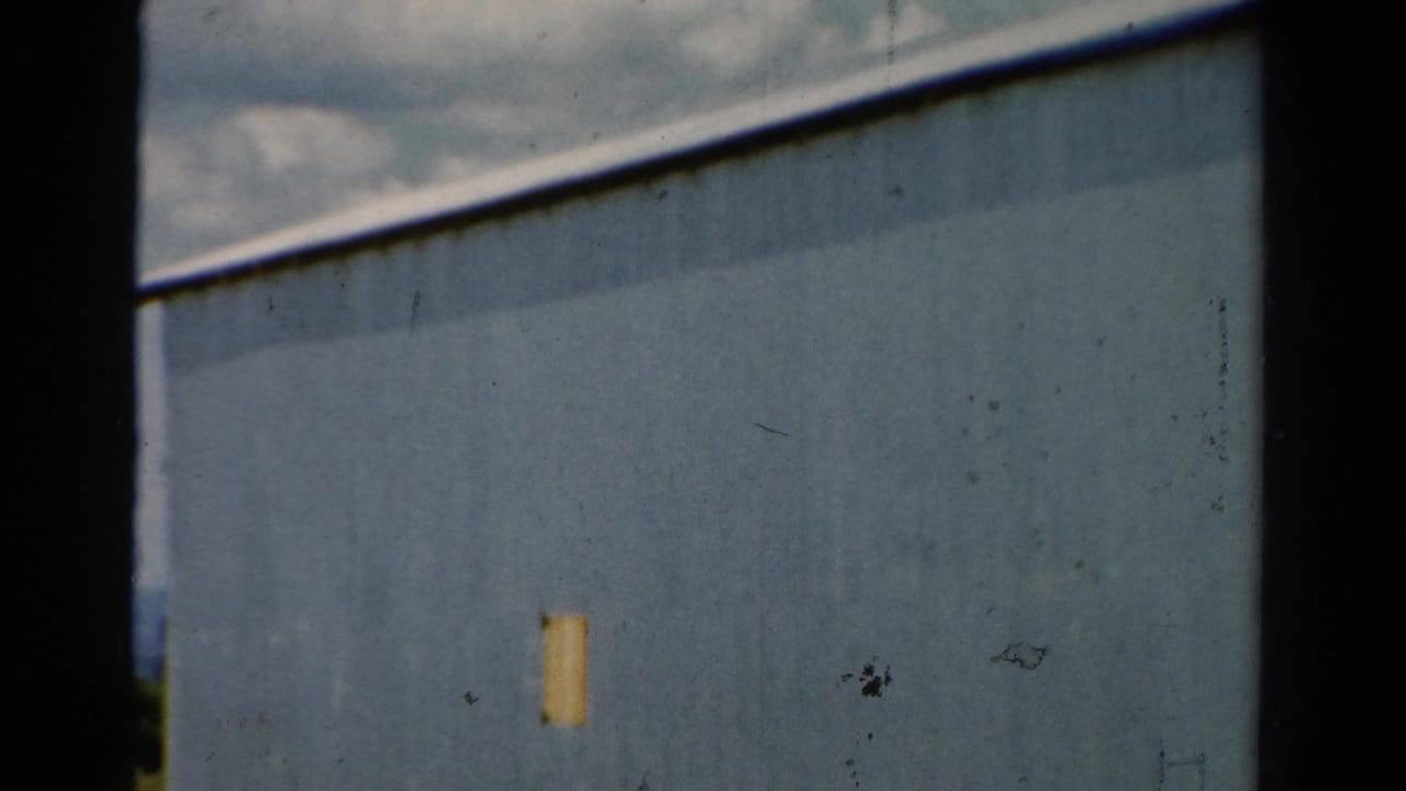 Blue metal-sided building seen close up with a small yellow patch and dark film borders.