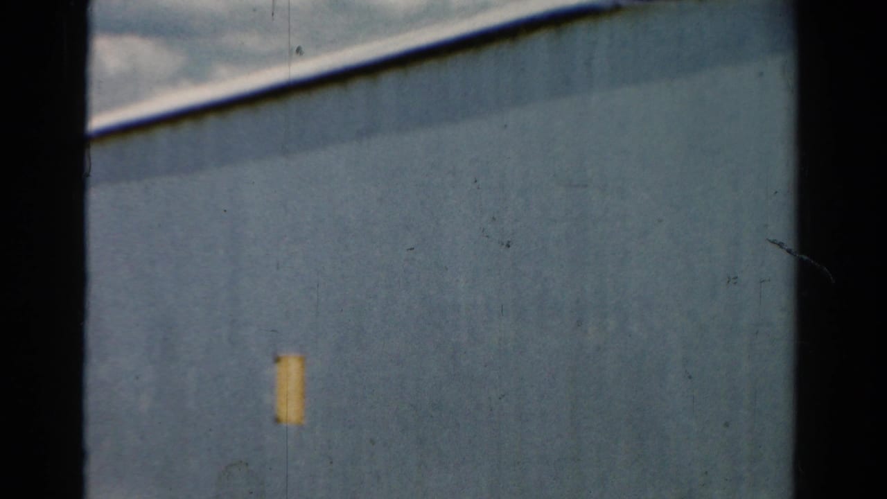 Close view of a blue building wall with a small yellow patch and dark vertical frame edge.