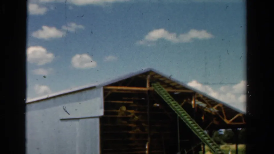 The final frame shows the rural barn's pale siding, exposed timber structure, and green diagonal equipment under a bright sky.