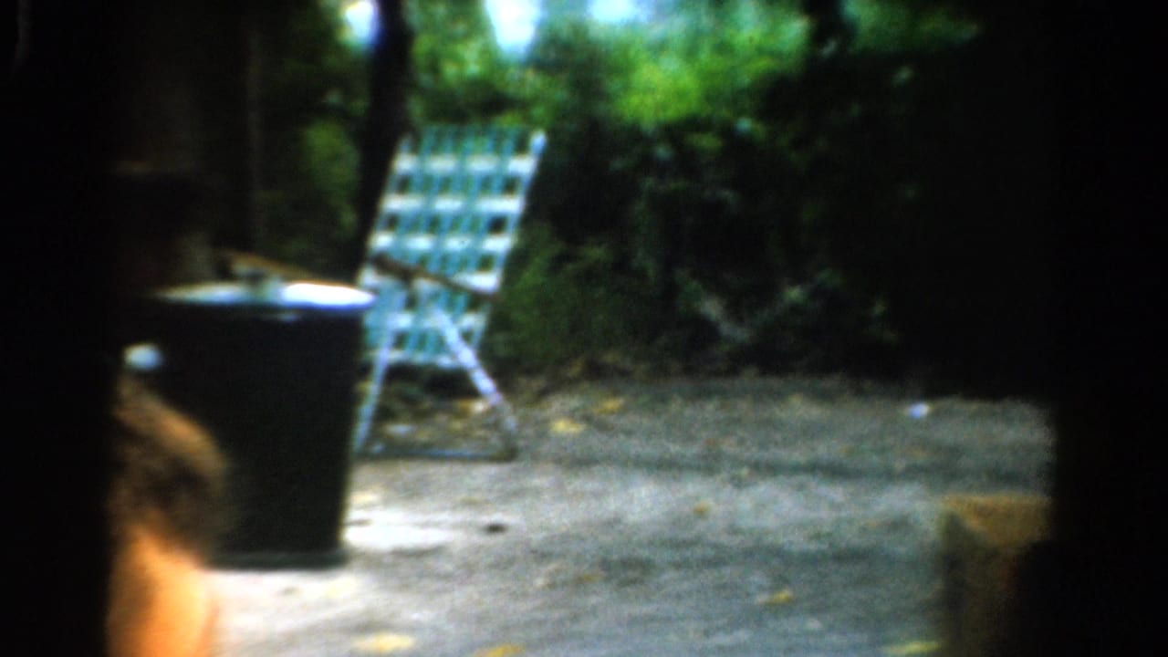 Checkered lawn chair and dark trash can on a shaded gravel outdoor area.