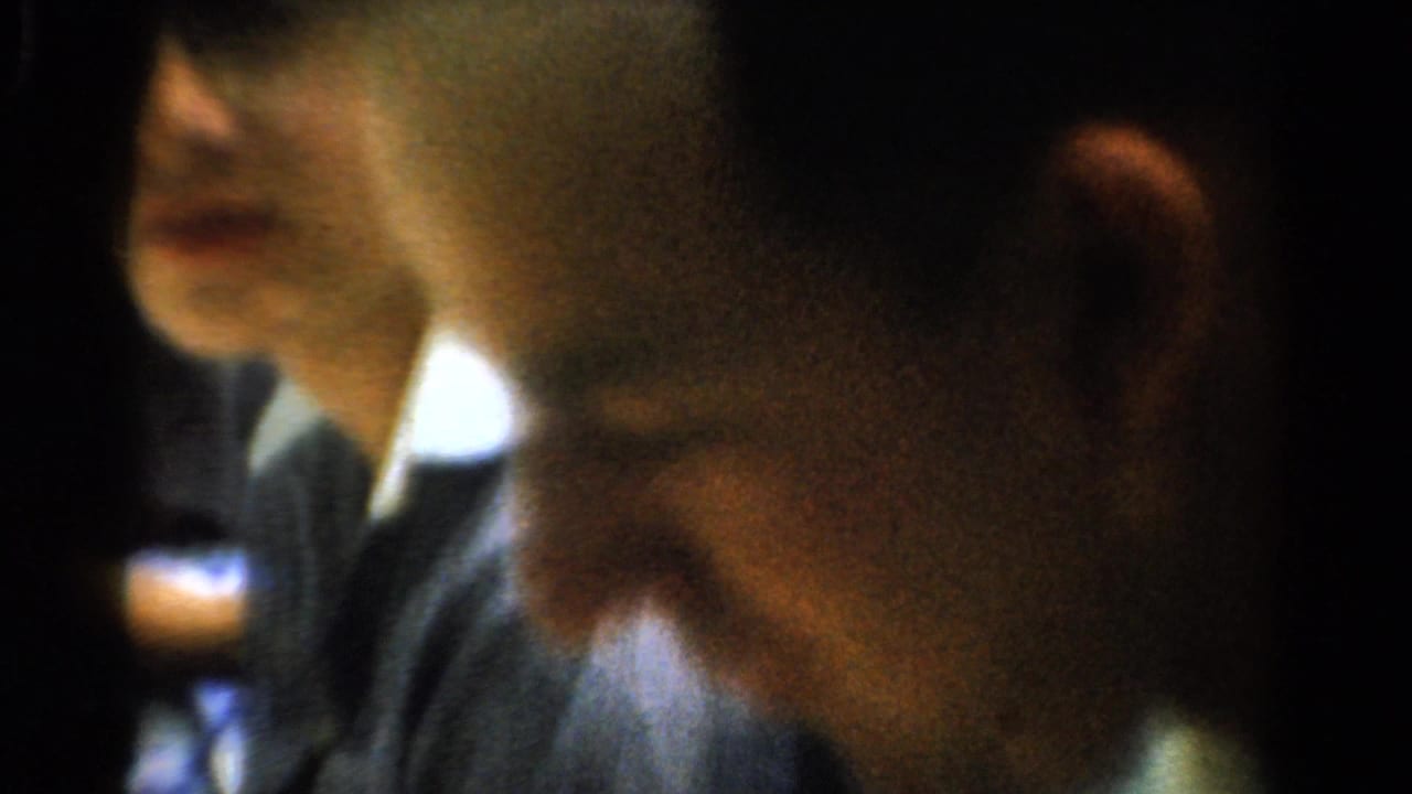 Close-up of an adult at a dim indoor table with another person in the background.