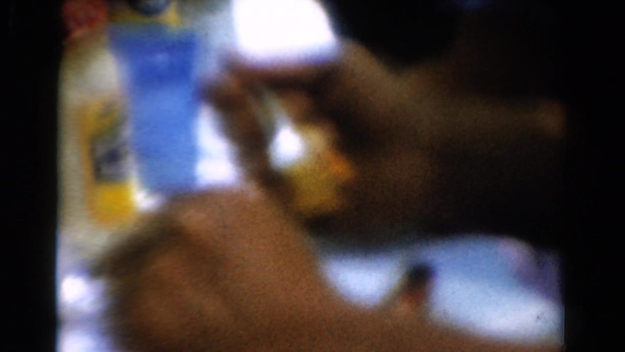 Soft-focus hand holding a fork near a plate with a blue bottle and yellow container behind it.