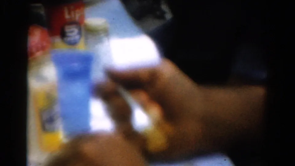 Grainy 8mm frame from the 1954 California clip showing a fork held near a plate in a casual tabletop scene.
