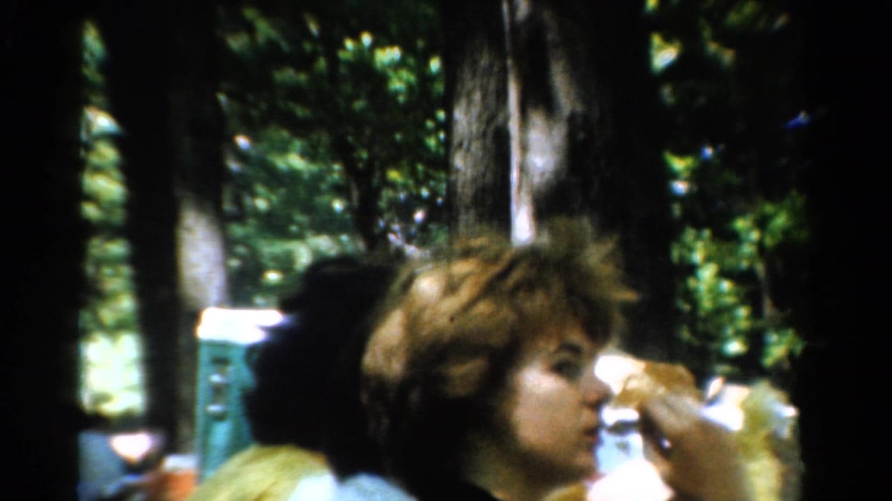 1954 California 8mm frame of adults at a wooded picnic table, with one person eating a sandwich in close foreground.