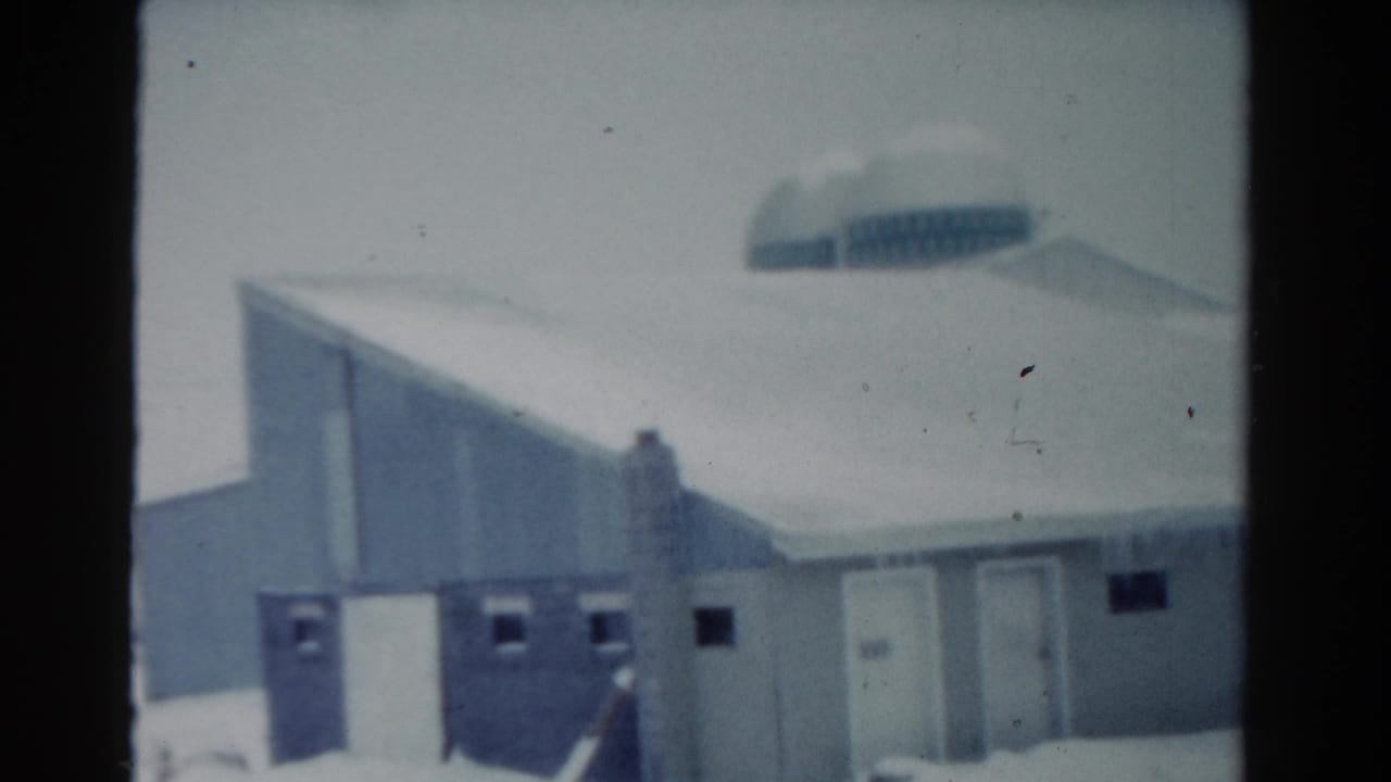 Snow-covered building exterior with icicles, doors, small windows, and a distant rounded roofline.