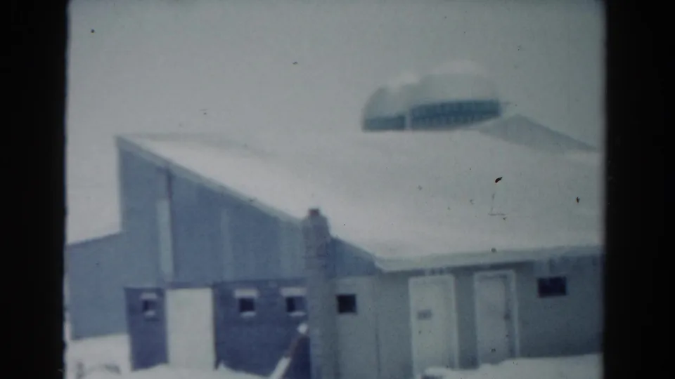1954 Toledo 8mm frame showing a snow-covered building exterior beneath a gray winter sky, with icicles and a distant rounded structure.