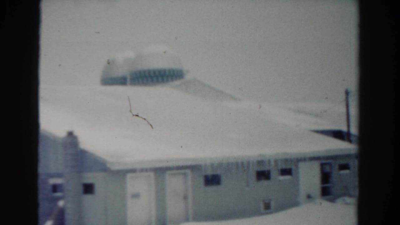 1954 Toledo 8mm frame showing a snow-covered low building with icicles along the eaves and a rounded background structure.
