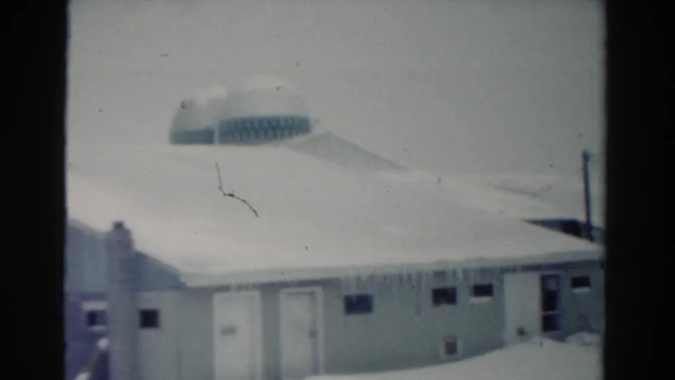 1954 Toledo 8mm frame showing a snow-covered low building with icicles along the eaves and a rounded background structure.