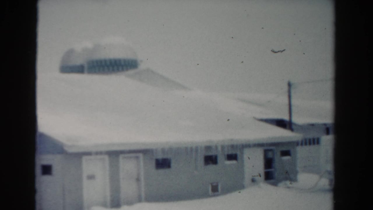 Snowy building exterior with doors, small windows, icicles, utility pole, and rounded background structure.