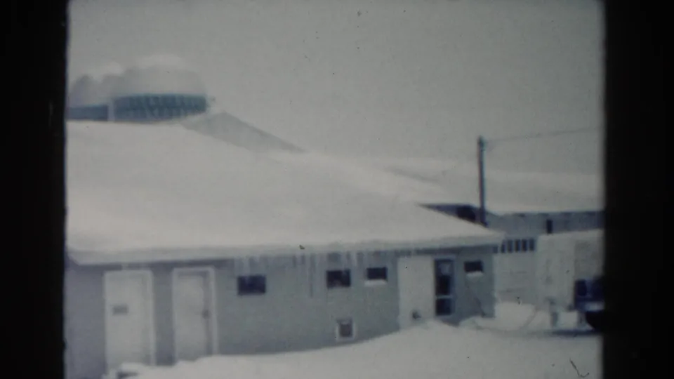 1954 Toledo 8mm frame holding on a low snow-covered building with icicles, doors, small windows, and a rounded background structure.