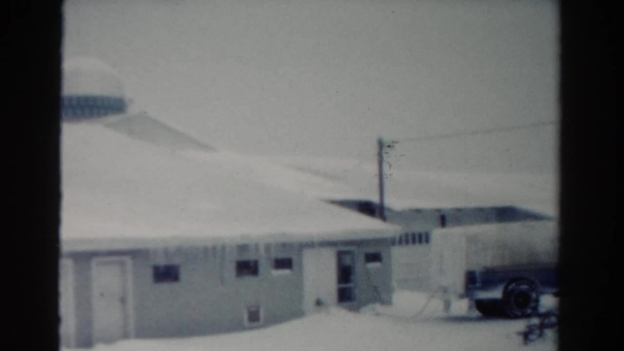 1954 Toledo home-movie frame showing a snow-covered low building, power pole, curved roofline, and part of a parked dairy truck.