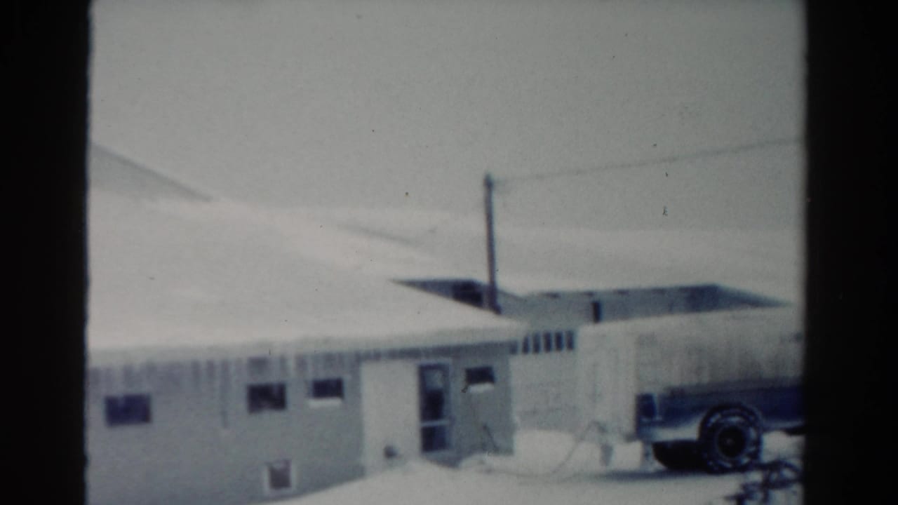 Snowy building exterior with a parked truck partly visible on the right.