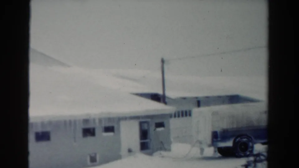 1954 Toledo frame of a low snow-covered building with windows, utility wires, and a parked Fairmen's Dairy truck partly visible.