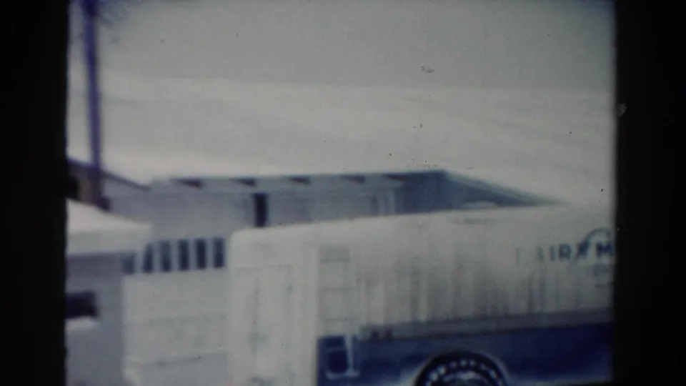 1954 Toledo home-movie frame with a Fairmen's Dairy truck body, rear wheel, snowbanks, and a low building behind it.
