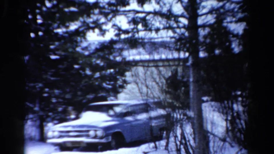 Blue-tinted 8mm frame of a light blue station wagon in a snowy Toledo exterior with trees and a building edge.
