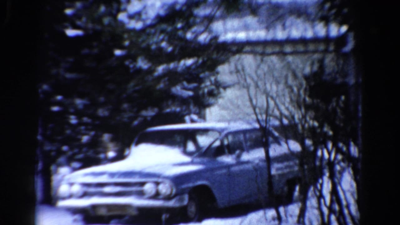 1954 Toledo home-movie frame showing a blue mid-century sedan partly obscured by bare trees and snow.