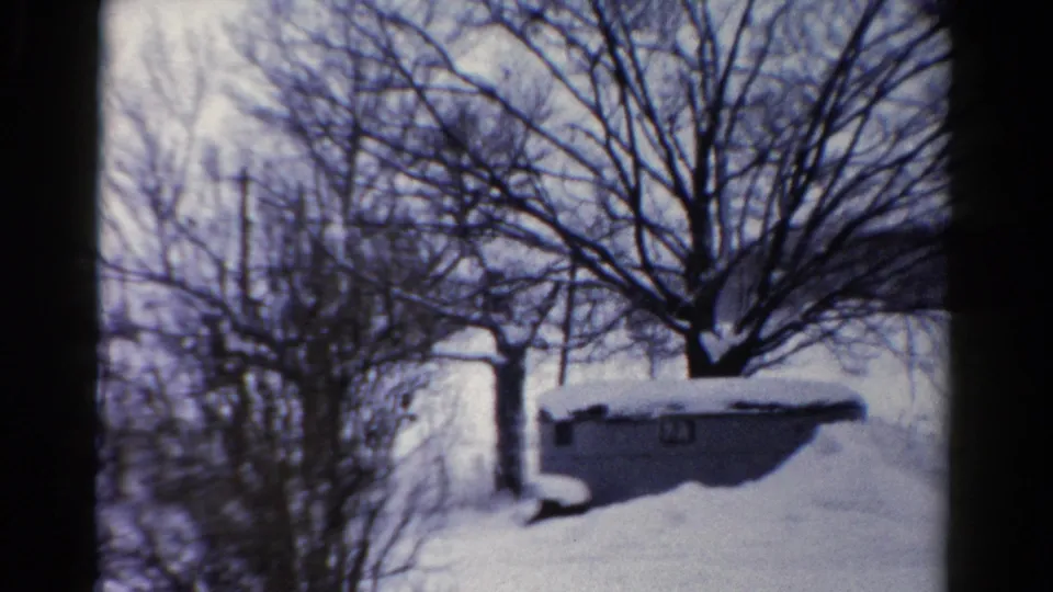 1954 Toledo home-movie view of a low shed covered in snow, framed by bare trees, shrubs, and a bright winter yard.