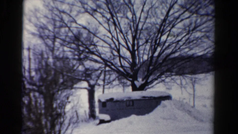 1954 Toledo, Ohio home-movie frame showing a snow-covered yard, small shed, bare trees, and open winter background.