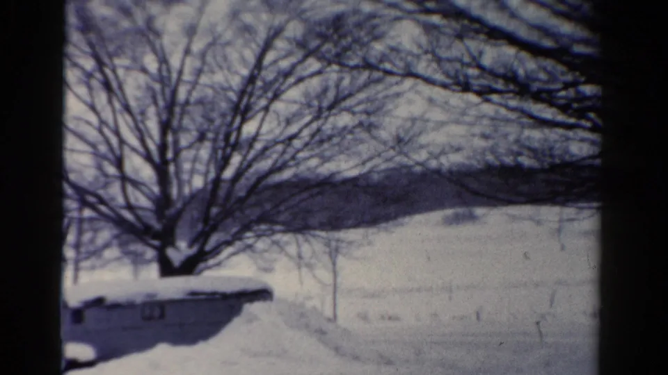 1954 Toledo 8mm frame showing snow-covered ground, bare tree branches, and a low structure partly buried in snow.
