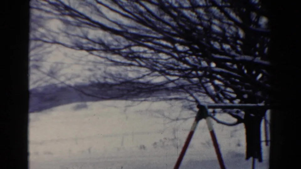 1954 Toledo 8mm frame showing a snow-covered yard, shadowed tree limbs, and the side of a swing set in a quiet winter view.