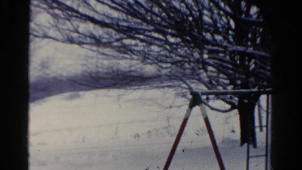 1954 Toledo winter home-movie still with a red and white swing set, leafless branches, and snow-covered ground under a pale sky.