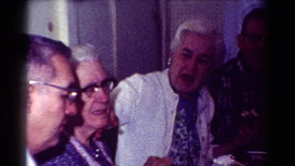 1954 Toledo home-movie frame showing older adults seated in a dim room, including a white-haired man facing forward.