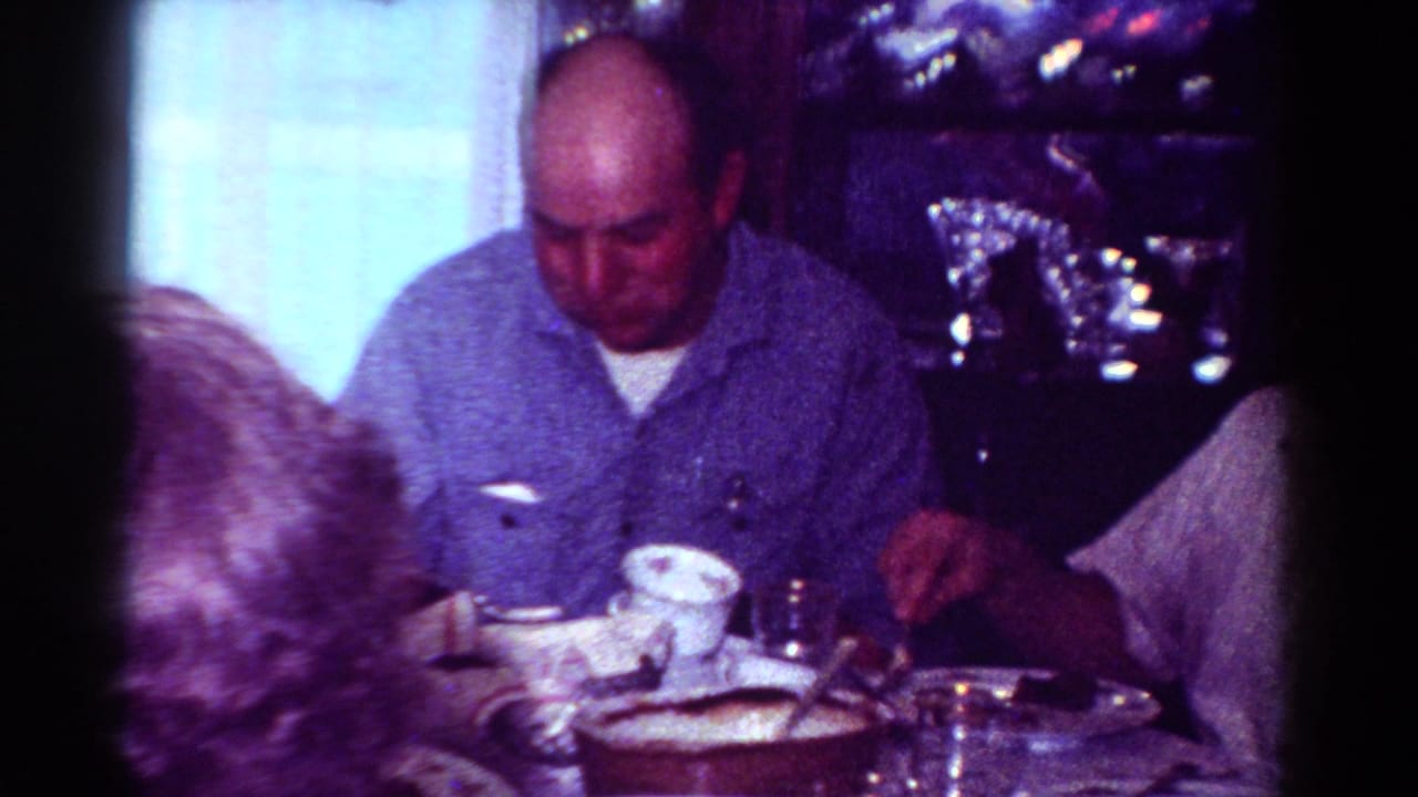 1954 Toledo home-movie frame showing adults eating at a dining table in a private interior.