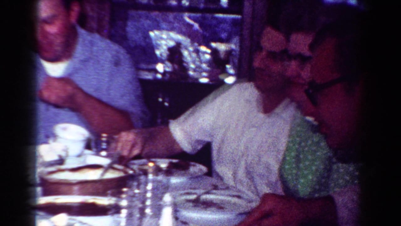 1954 Toledo home-movie frame of adults eating and conversing at a crowded dinner table.