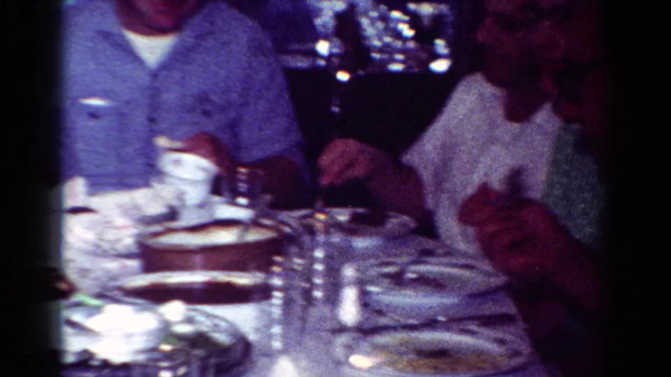 1954 Toledo home-movie frame of adults eating at a private dinner table with soft, tinted film color.