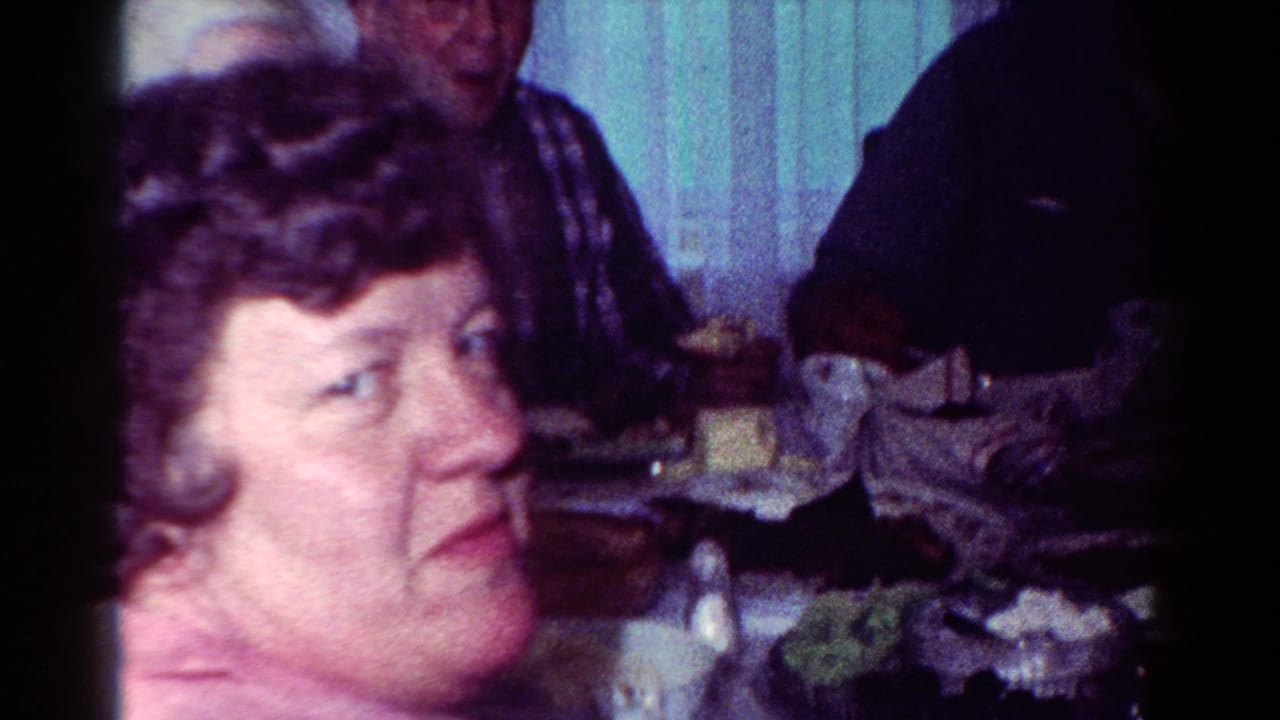 A woman in a pink top is seen close to the camera as adults continue eating at a dining table in a 1954 Toledo home interior.