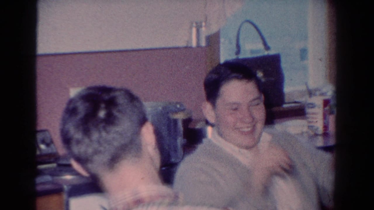Two adult men appear in a 1954 Toledo kitchen, with one smiling broadly as another turns toward him in the foreground.