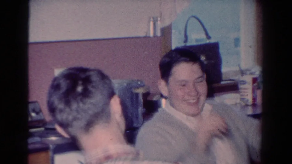 Two adult men appear in a 1954 Toledo kitchen, with one smiling broadly as another turns toward him in the foreground.